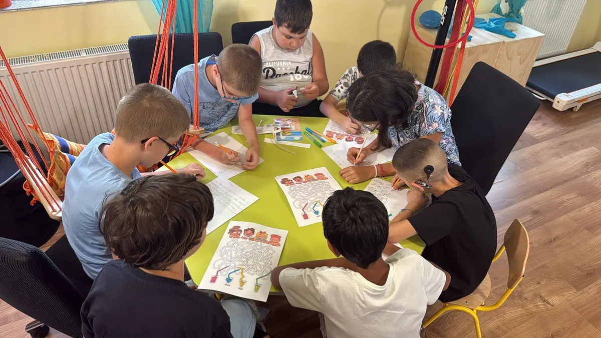Copii care desenează împreună la o masă, într-un atelier al asociației
